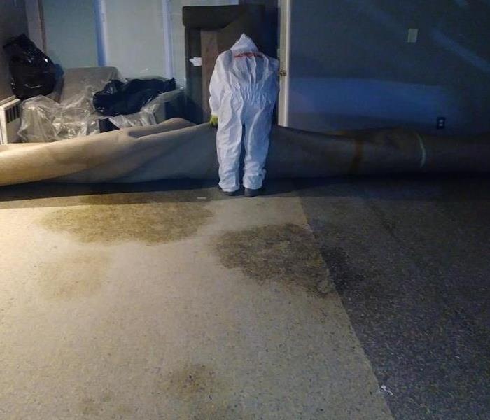 SERVPRO crew member rolling damaged carpet to expose wet flooring.